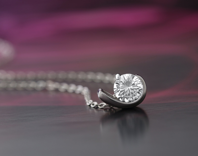 Image of a stylish single diamond necklace on a blurred red and grey background